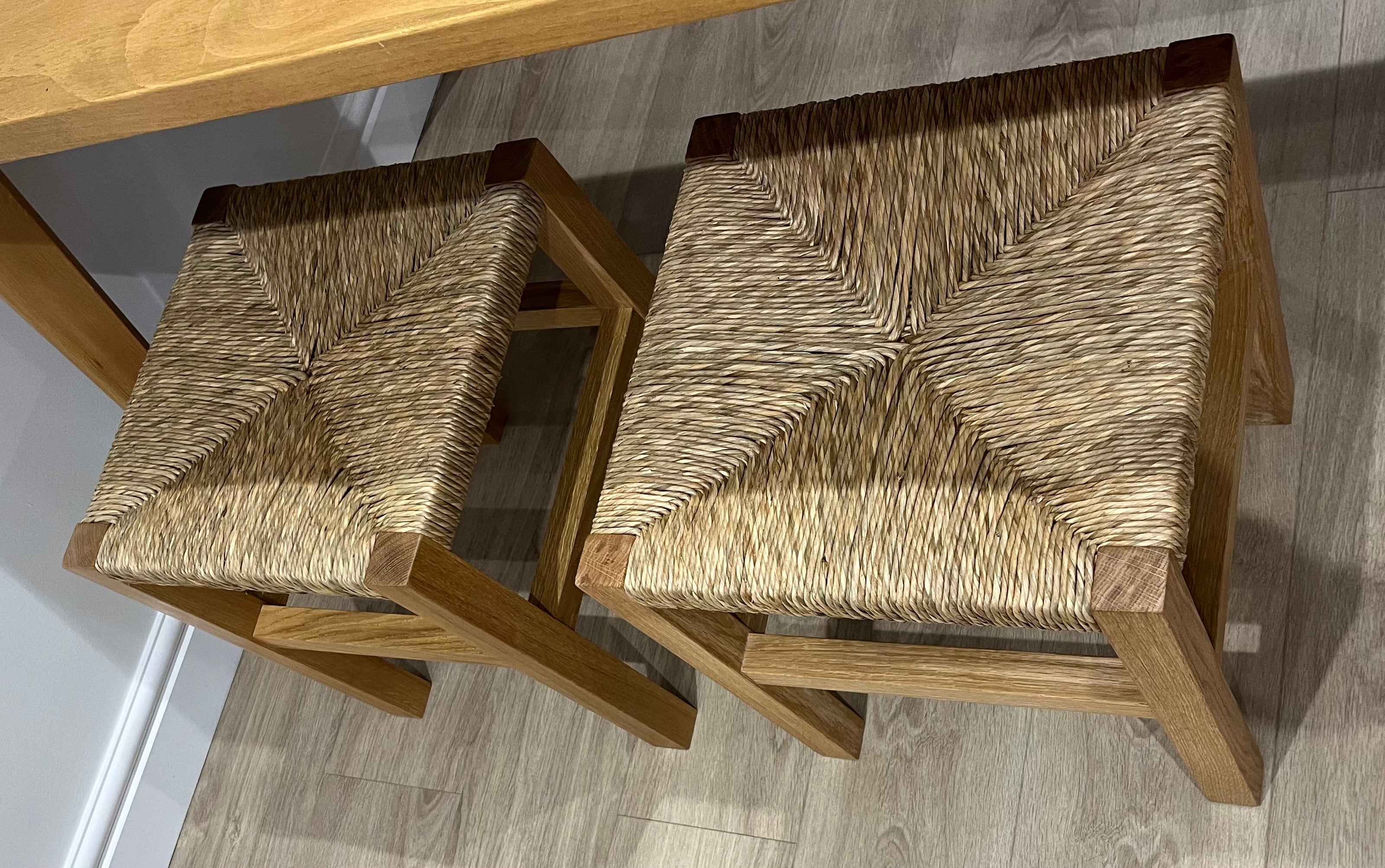 Close up detail of a pair of solid oak handcrafted stools, with hand-woven rush seats, on wooden floor, at dining table