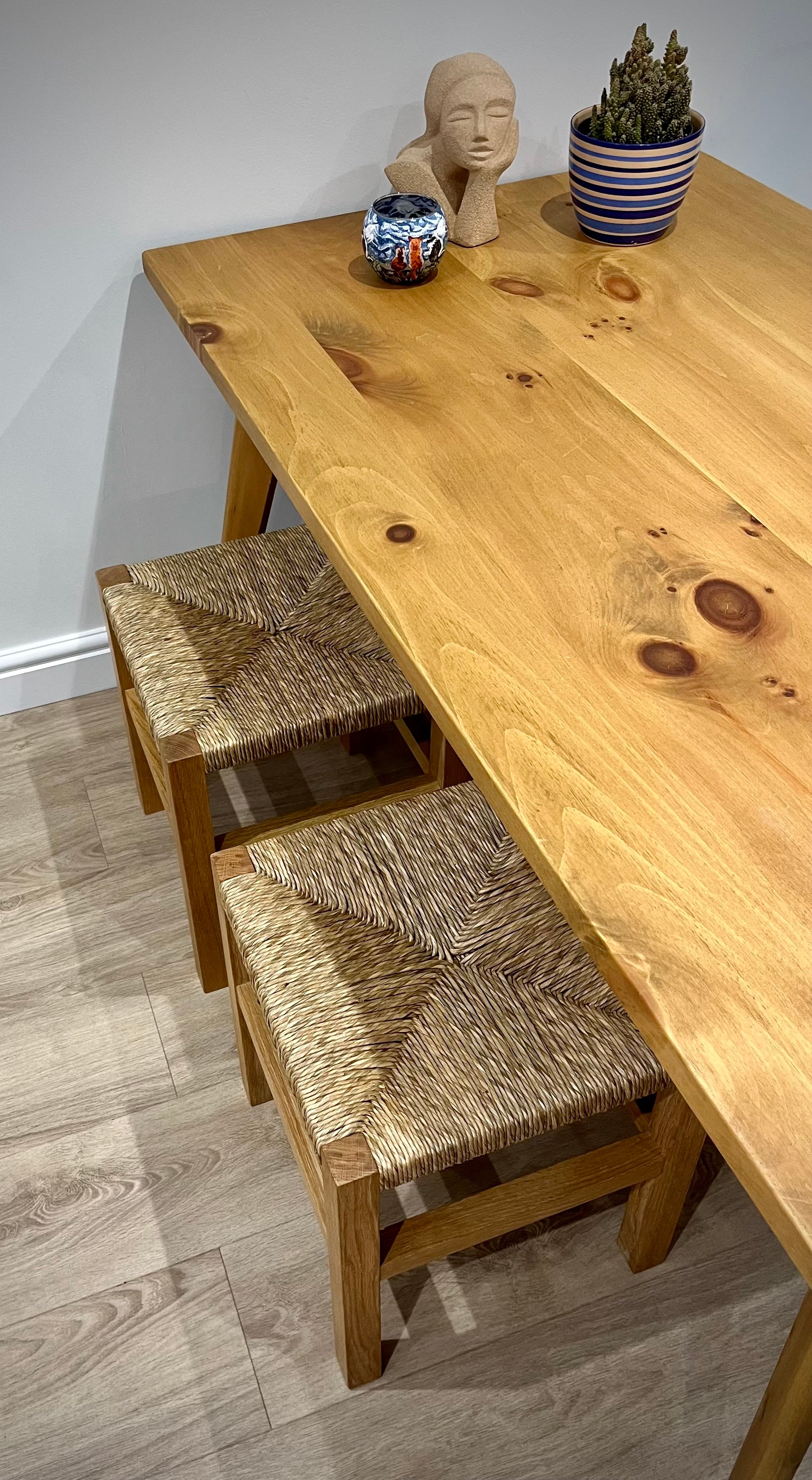 Two handcrafted solid oak stools with natural rush seats at a dining table 